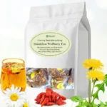 Product shot of a white resealable pouch labeled "Dandelion Wolfberry Tea" for "Clearing Heat & Detoxifying" and "Maintaining kidney and liver health." In the foreground are a glass of brewed tea, fresh yellow dandelion flowers, a white chamomile-like flower, and a pile of red wolfberries (Goji berries). The packaging shows a window revealing individual sealed tea packets inside.